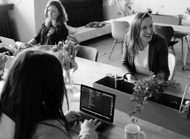 Three women working on laptops in an office environment with tables and chairs